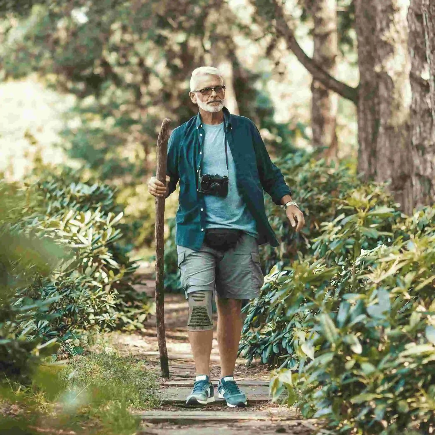 Knee sleeve worn by an older man hiking on a wooded trail with a walking stick.